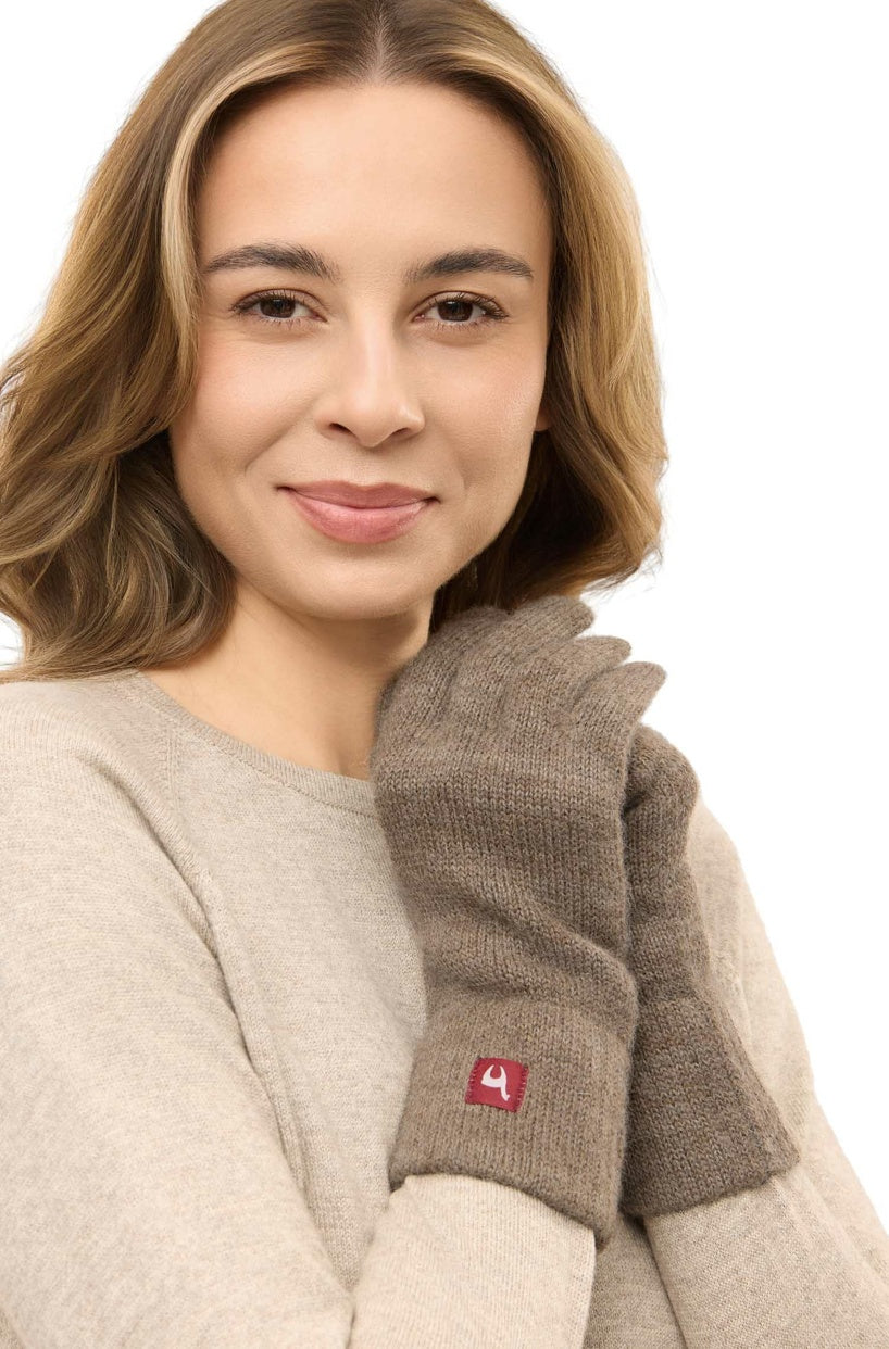 Eine Frau trägt braune Apu Kuntur – Alpaka Fingerhandschuhe Uni – fingerlose Handschuhe aus 100 % Baby-Alpaka mit einem kleinen roten Logo-Etikett am Handgelenk.